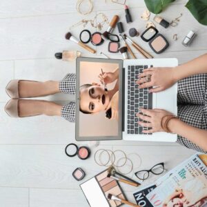 Student working on laptop surrounded by makeup and magazines