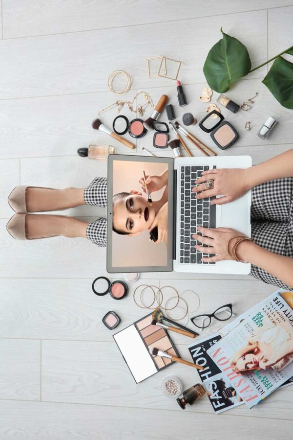 Student working on laptop surrounded by makeup and magazines